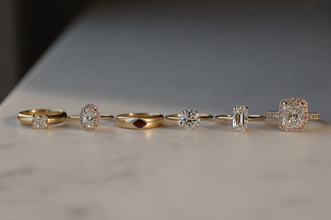 A row of five diamond engagement rings in 18ct gold showing different settings on a marble surface