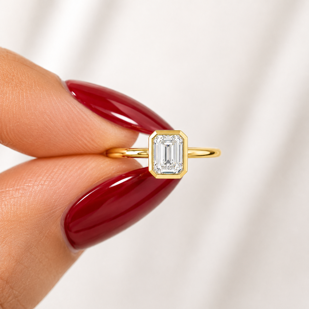 Close-up of an emerald-cut lab-grown diamond bezel-set solitaire engagement ring in yellow gold